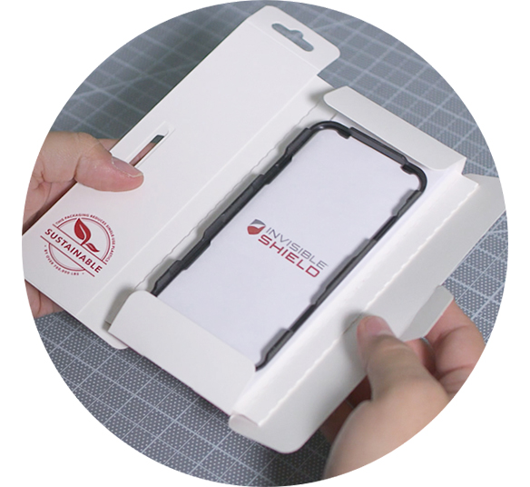 Hands unboxing an InvisibleShield screen protector in sustainable packaging with EZ Apply tray