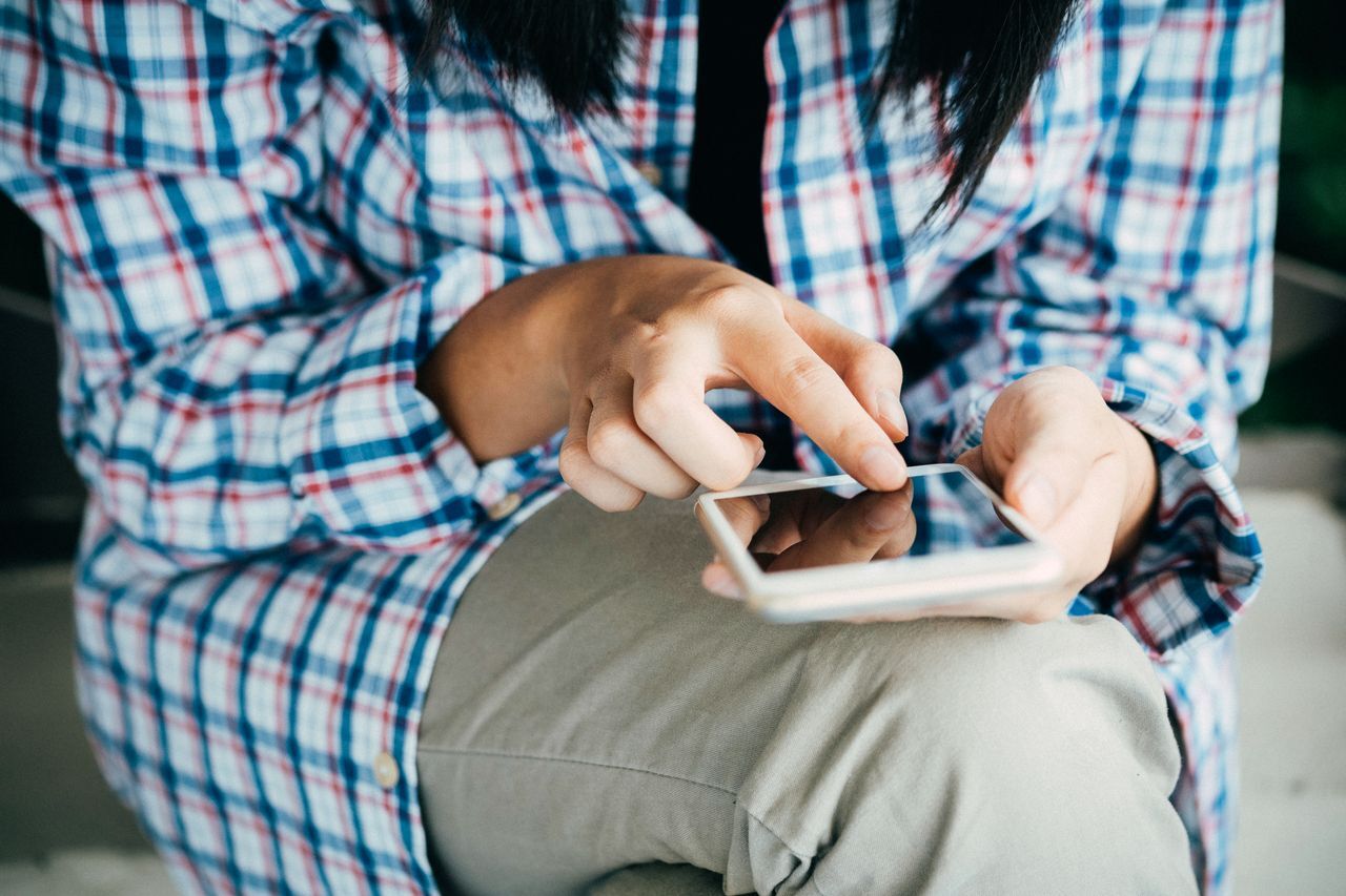 person in plaid shirt sitting and using a smartphone