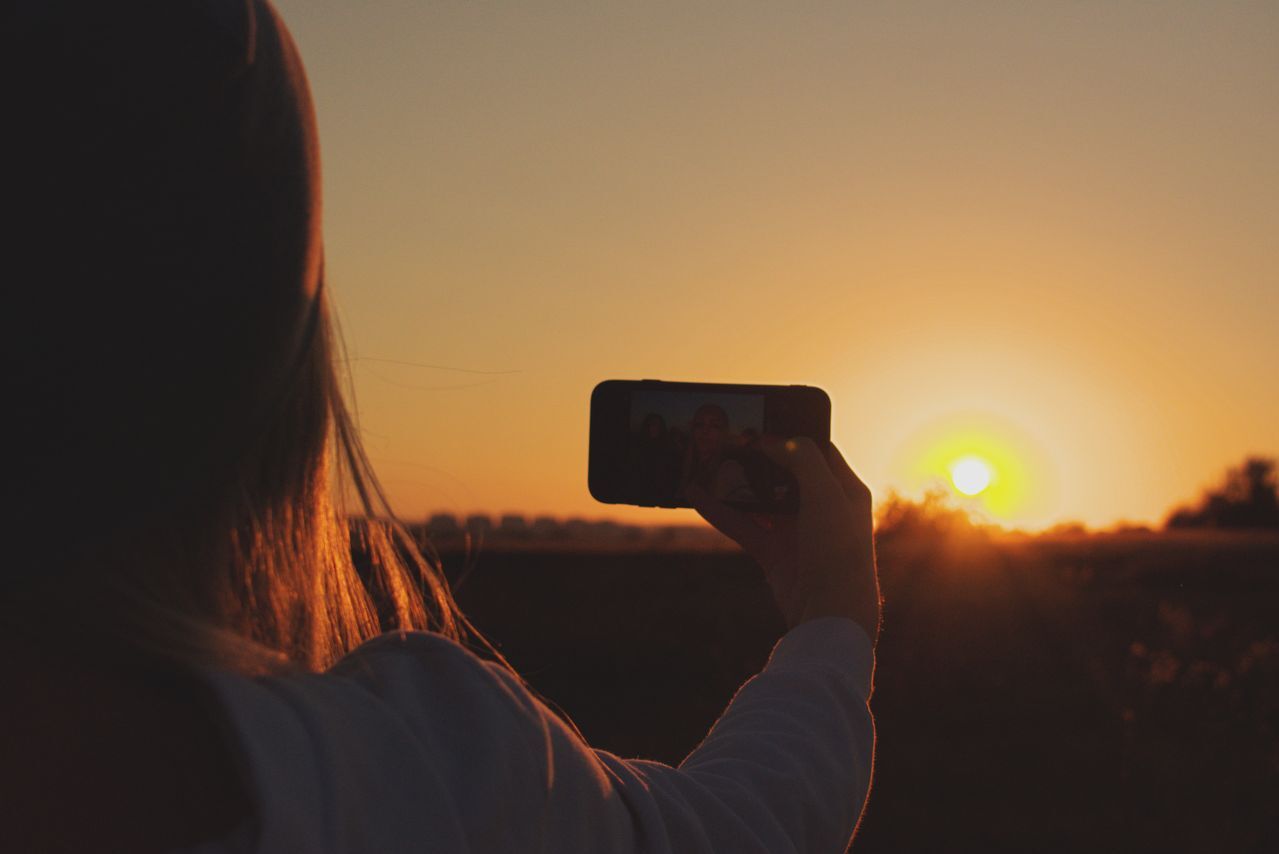 Woman taking a photo of a sunset on her phone