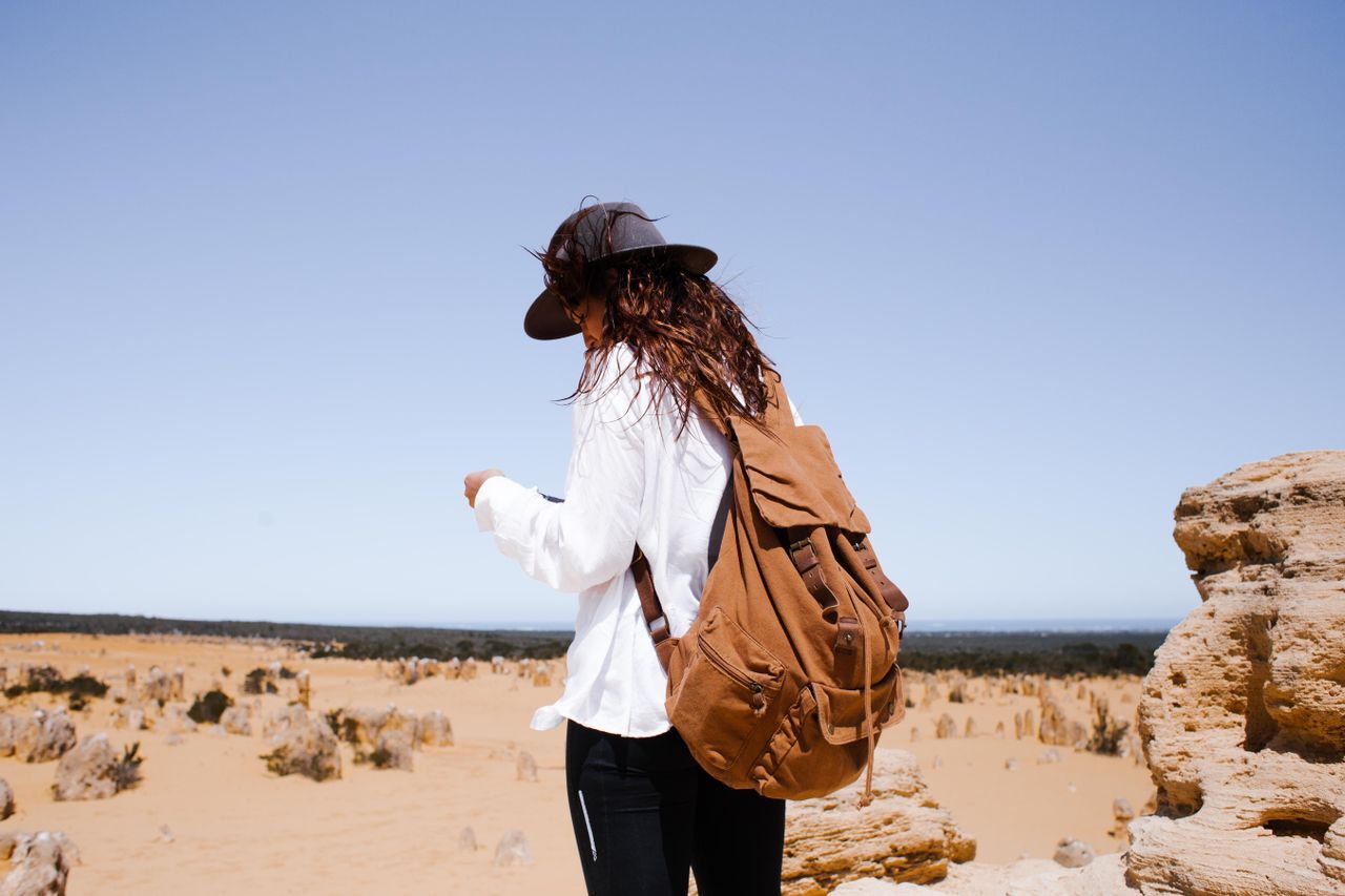 woman with long sleeved white shirt and hat looking at device in the desert